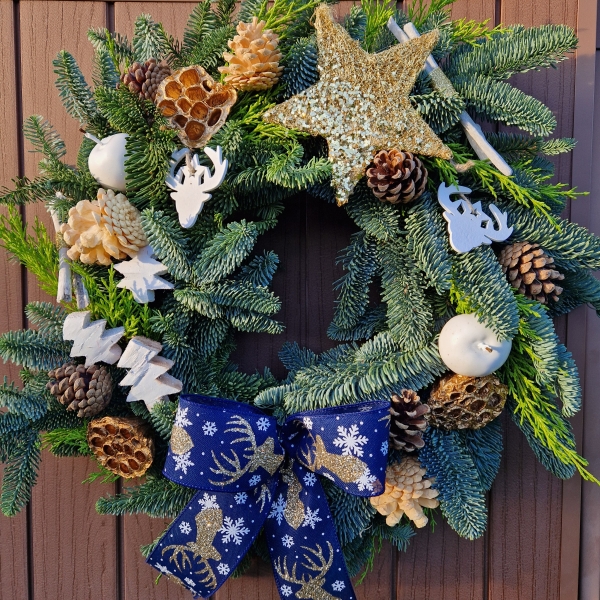 White and gold Christmas wreath with navy stag ribbon, gold sisal star, white coco trees, pine cones, lotus pods, waxed apples, and fresh pine on a moss ring.