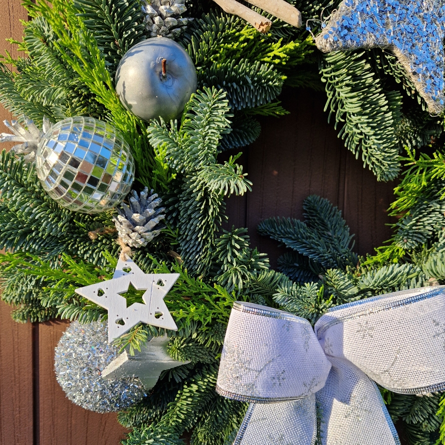 Christmas door wreath with fresh pine, conifers, silver sisal star, wooden and coco stars, waxed apples, pine cones, and mirror baubles.