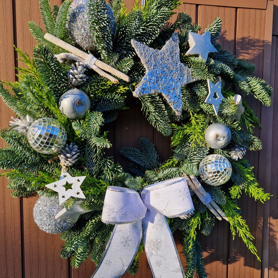 Christmas door wreath with fresh pine, conifers, silver sisal star, wooden and coco stars, waxed apples, pine cones, and mirror baubles.