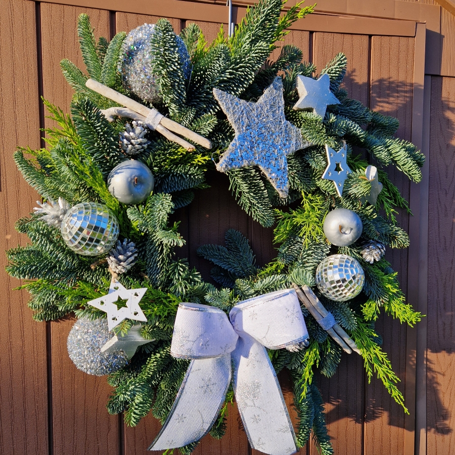 Christmas door wreath with fresh pine, conifers, silver sisal star, wooden and coco stars, waxed apples, pine cones, and mirror baubles.