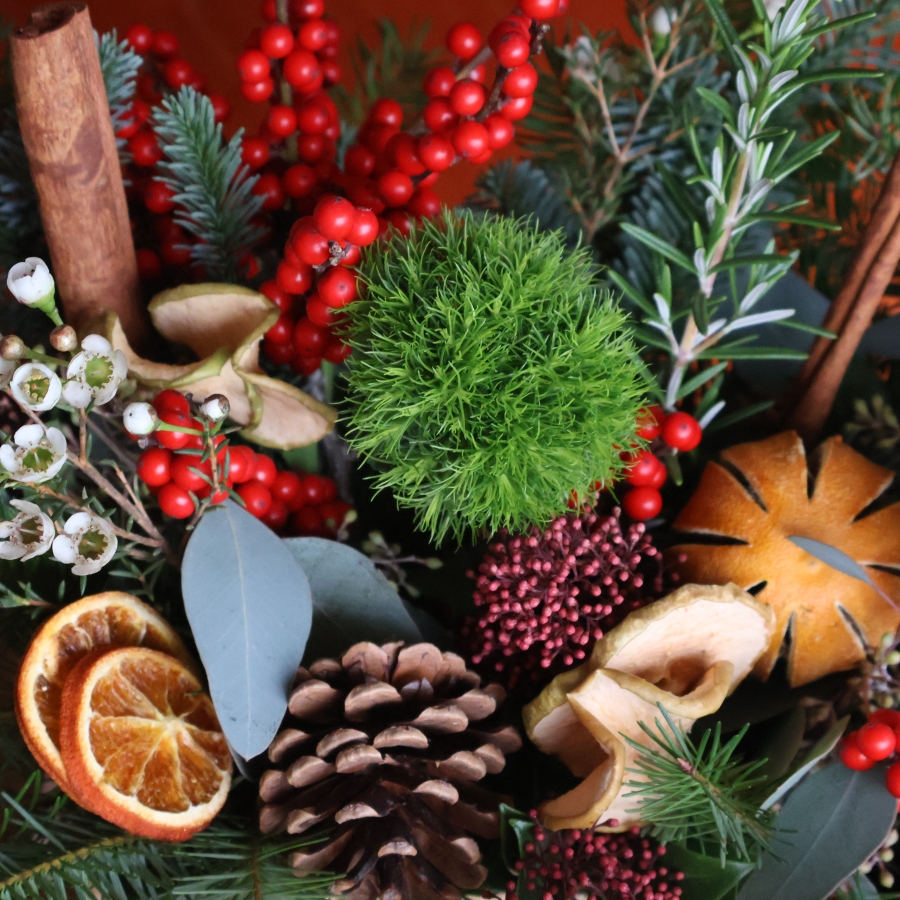 Winter arrangement in a hessian trough with pine, ilex berries, dried oranges, cinnamon sticks, pine cones, wax flower, and natural foliage.