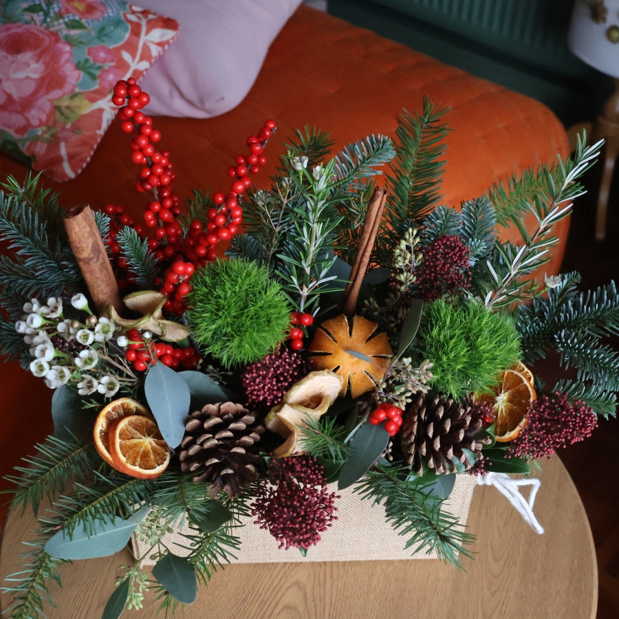 Winter arrangement in a hessian trough with pine, ilex berries, dried oranges, cinnamon sticks, pine cones, wax flower, and natural foliage.