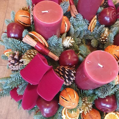 Luxury Christmas advent wreath with four burgundy pillar candles, velvet bows, fresh Nobilis pine, pine cones, cinnamon sticks, dried orange and apple slices, chillies, and waxed apples