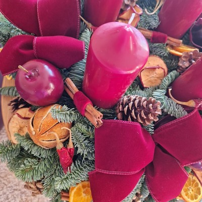 Luxury Christmas advent wreath with four burgundy pillar candles, velvet bows, fresh Nobilis pine, pine cones, cinnamon sticks, dried orange and apple slices, chillies, and waxed apples