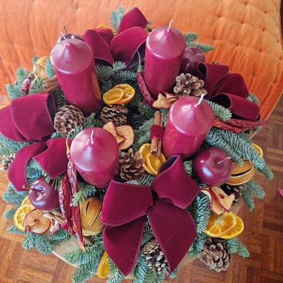 Luxury Christmas advent wreath with four burgundy pillar candles, velvet bows, fresh Nobilis pine, pine cones, cinnamon sticks, dried orange and apple slices, chillies, and waxed apples