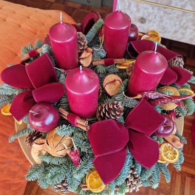 Luxury Christmas advent wreath with four burgundy pillar candles, velvet bows, fresh Nobilis pine, pine cones, cinnamon sticks, dried orange and apple slices, chillies, and waxed apples