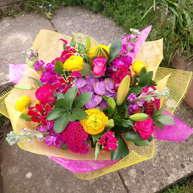 Brighton Bloom summer bouquet featuring vivid gloriosa, hot pink roses and celosia, golden achillea, purple scented matthiola, and large hydrangea—arranged with dramatic colour contrasts - inspired by a vibrant seafront.