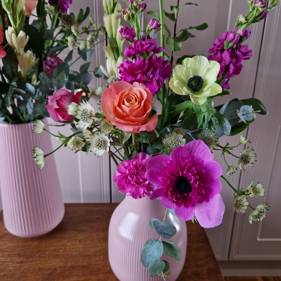 A spring arrangement in a matt pink ceramic vase featuring matthiola, tuberose, allium, roses, carnations, and anemones in fuchsia, apricot, yellow, and pink tones, styled in a natural Floramay design.