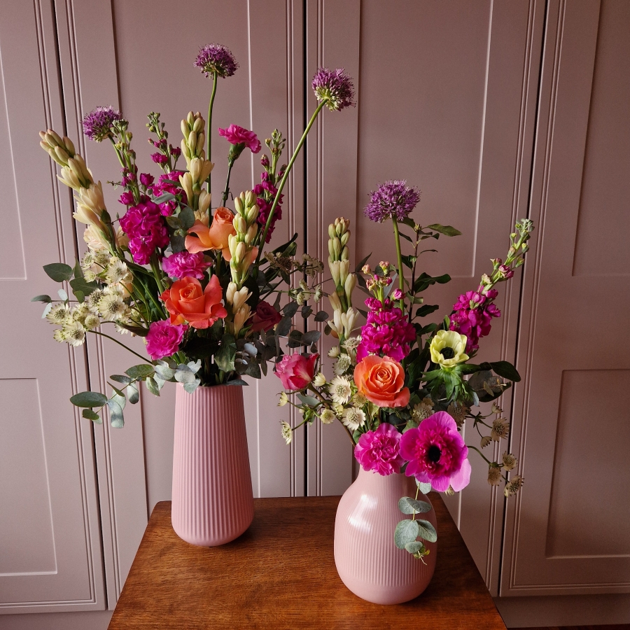 A spring arrangement in a matt pink ceramic vase featuring matthiola, tuberose, allium, roses, carnations, and anemones in fuchsia, apricot, yellow, and pink tones, styled in a natural Floramay design.
