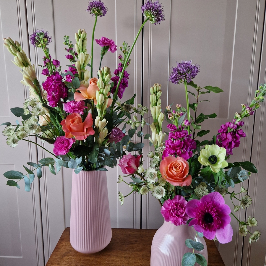 A spring arrangement in a matt pink ceramic vase featuring matthiola, tuberose, allium, roses, carnations, and anemones in fuchsia, apricot, yellow, and pink tones, styled in a natural Floramay design.