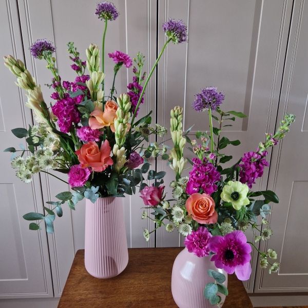 A spring arrangement in a matt pink ceramic vase featuring matthiola, tuberose, allium, roses, carnations, and anemones in fuchsia, apricot, yellow, and pink tones, styled in a natural Floramay design.