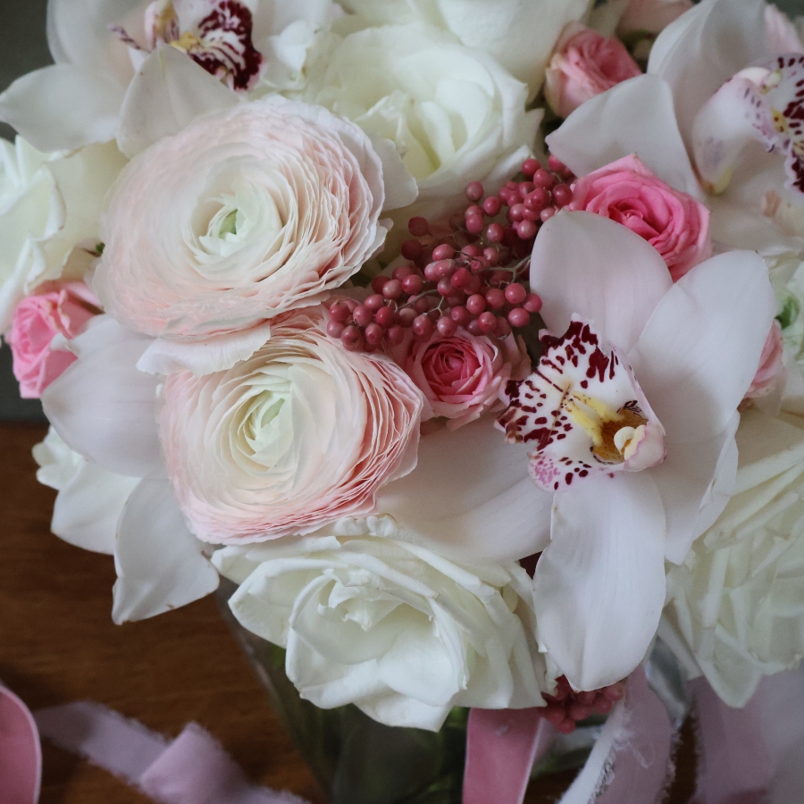 A luxury cube‑vase arrangement with white hydrangea, pale pink Cloni ranunculus, pink spray roses, white roses, white cymbidium orchid heads and pink pepperberries.