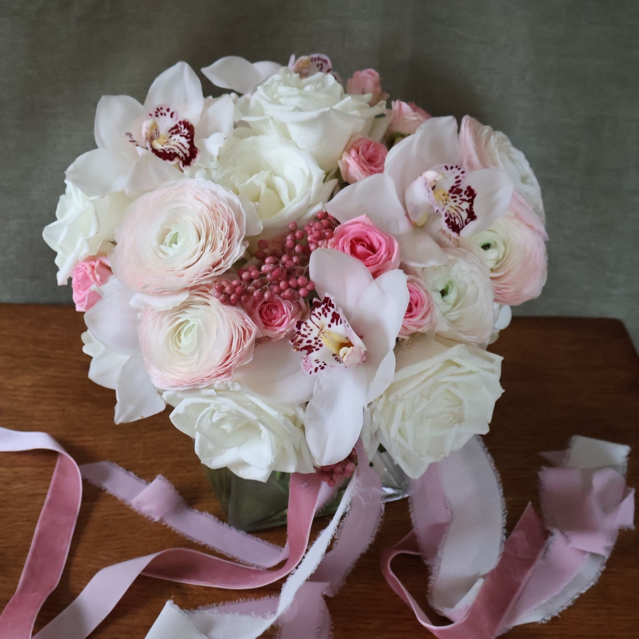 A luxury cube‑vase arrangement with white hydrangea, pale pink Cloni ranunculus, pink spray roses, white roses, white cymbidium orchid heads and pink pepperberries.