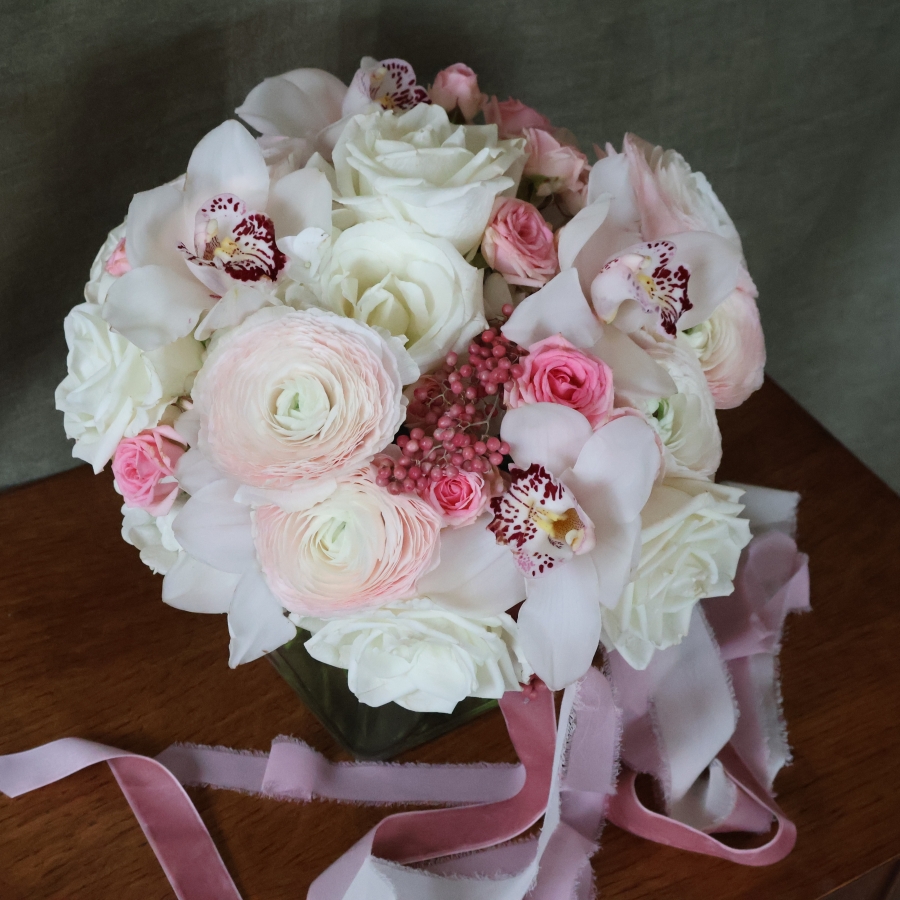 A luxury cube‑vase arrangement with white hydrangea, pale pink Cloni ranunculus, pink spray roses, white roses, white cymbidium orchid heads and pink pepperberries.