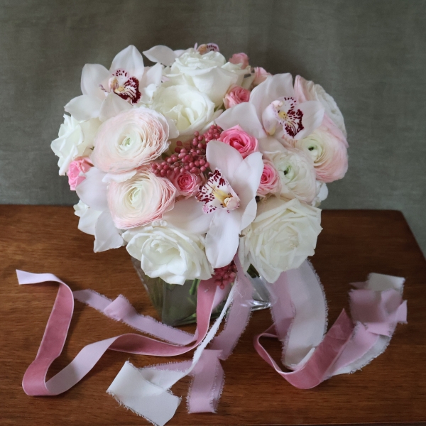 A luxury cube‑vase arrangement with white hydrangea, pale pink Cloni ranunculus, pink spray roses, white roses, white cymbidium orchid heads and pink pepperberries.