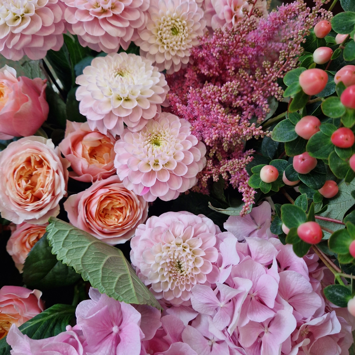 Borde Hill bouquet with pink hydrangeas, apricot garden roses, berries and astilbe displayed in a clear glass vase