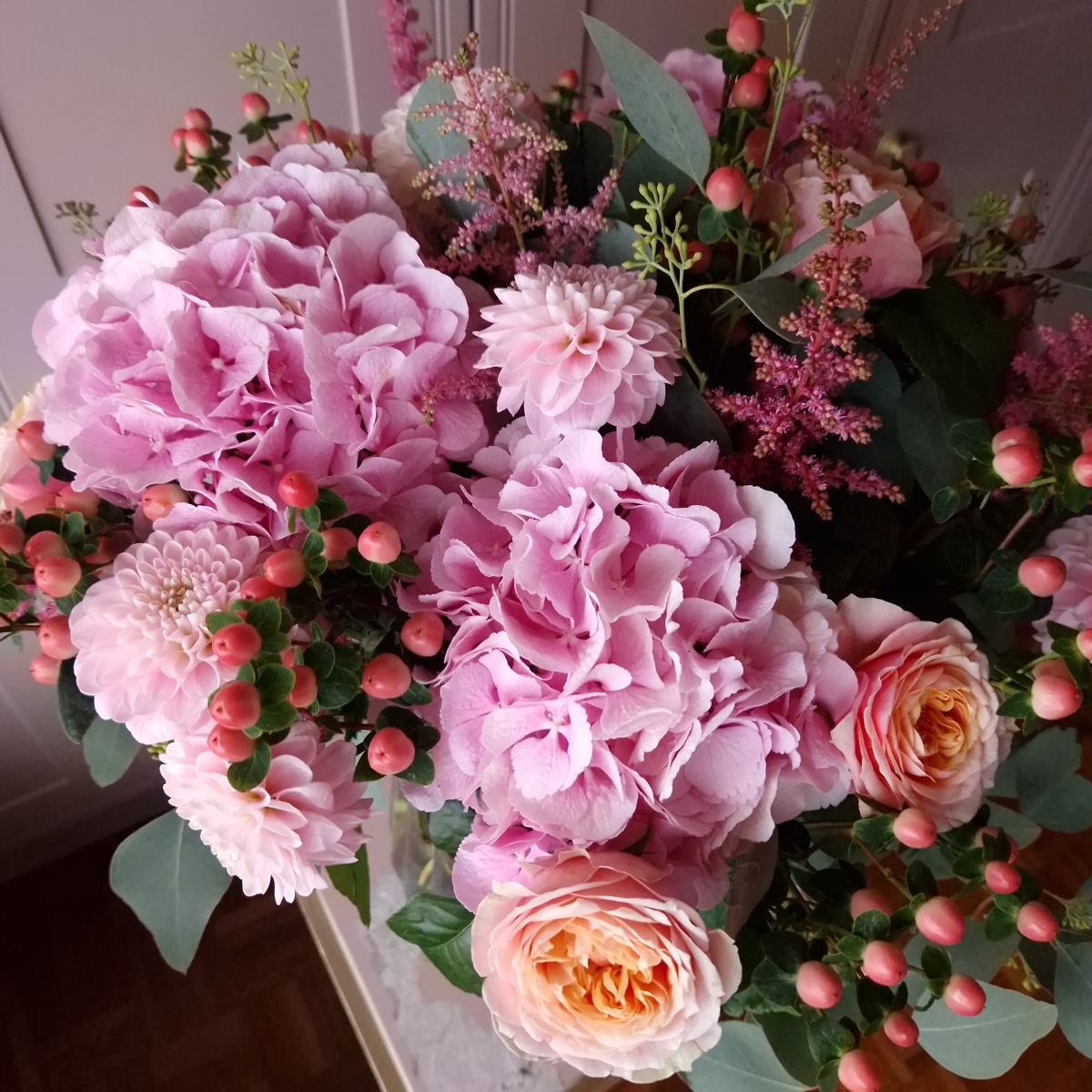 Borde Hill bouquet with pink hydrangeas, apricot garden roses, berries and astilbe displayed in a clear glass vase