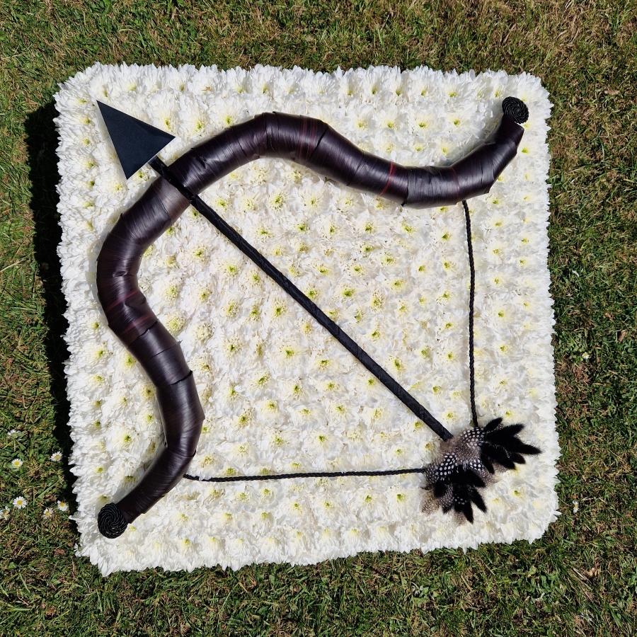 Bespoke funeral wreath with bow and arrow design made from black tie leaves on white chrysanthemum base
