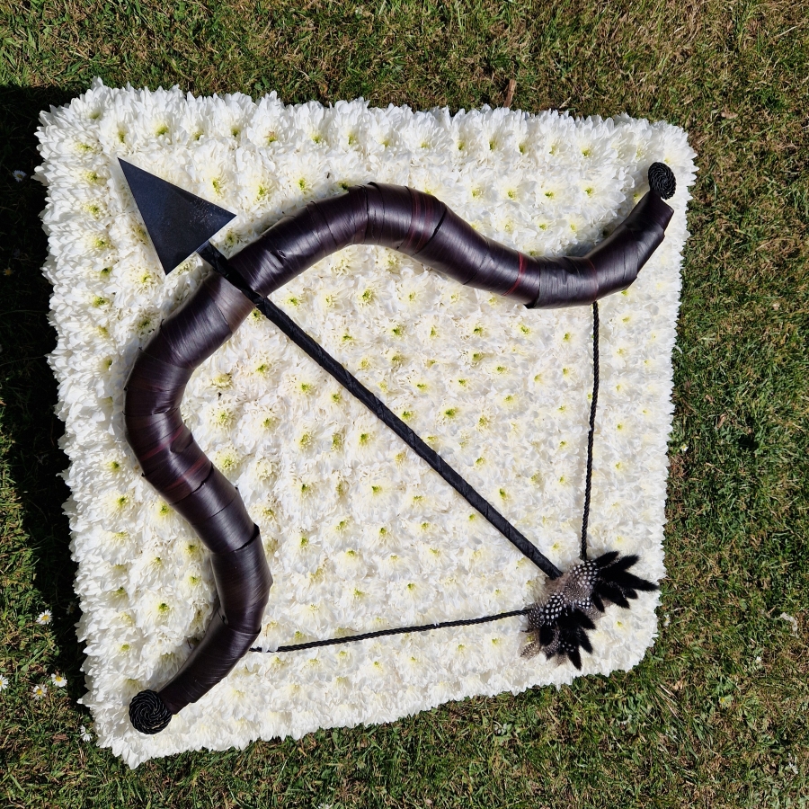 Bespoke funeral wreath with bow and arrow design made from black tie leaves on white chrysanthemum base