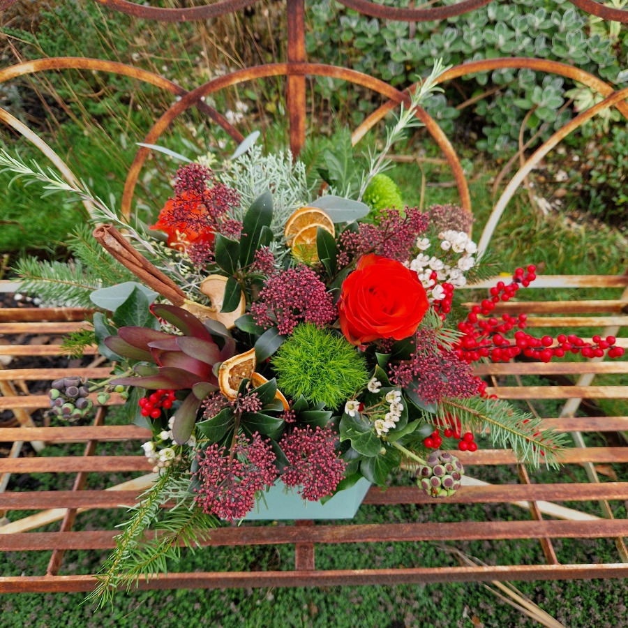 Christmas hat box arrangement with burnt orange roses, burgundy Skimmia, wax flower, ilex berries, pine, ivy berries, dried oranges, cinnamon sticks, and pine cones