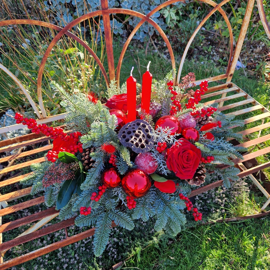 Crimson Eve Christmas centrepiece with red candles, deep red roses, fresh pine, waxed apples, pine cones, red baubles, and ilex berries