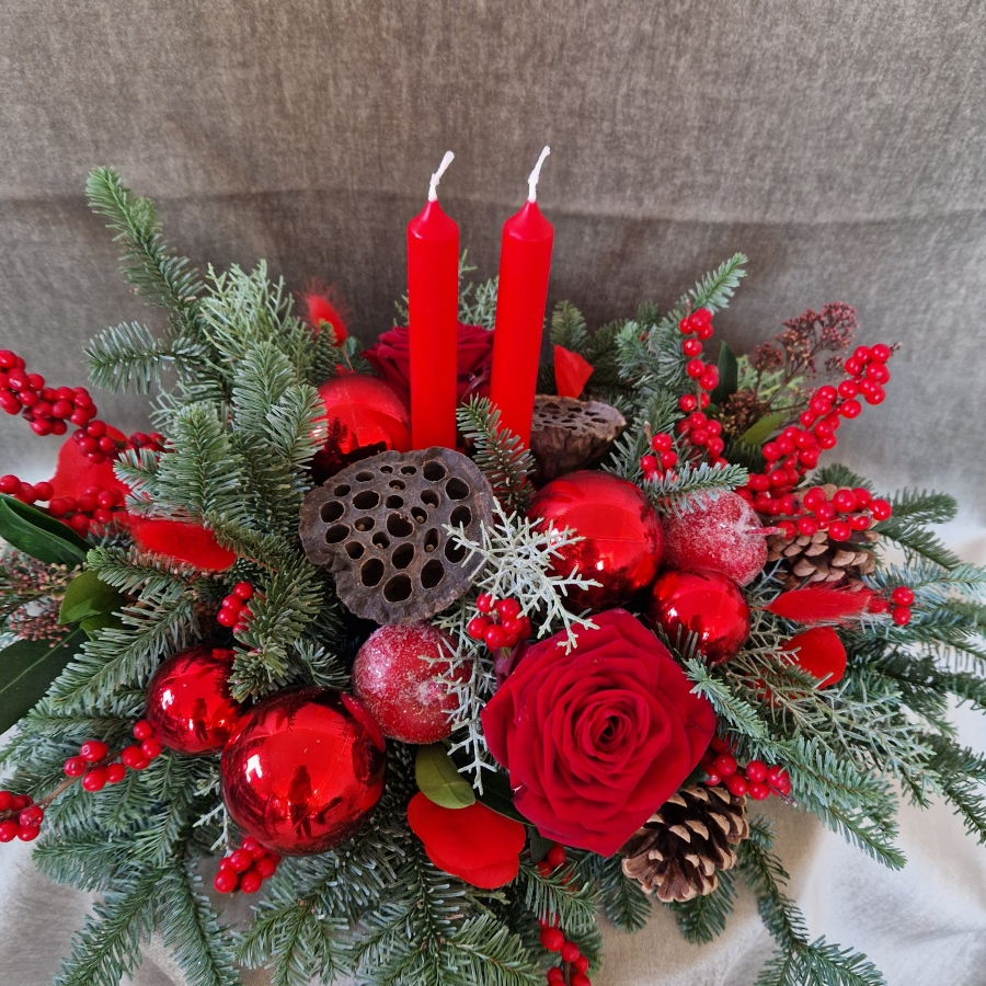 Crimson Eve Christmas centrepiece with red candles, deep red roses, fresh pine, waxed apples, pine cones, red baubles, and ilex berries