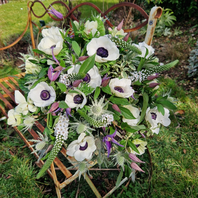 Spring bouquet with white Mistral Anemones, purple Clematis, Lysimachia, and white sea holly, inspired by East Dean’s cottage gardens and coastal charm.