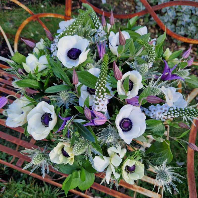 Spring bouquet with white Mistral Anemones, purple Clematis, Lysimachia, and white sea holly, inspired by East Dean’s cottage gardens and coastal charm.