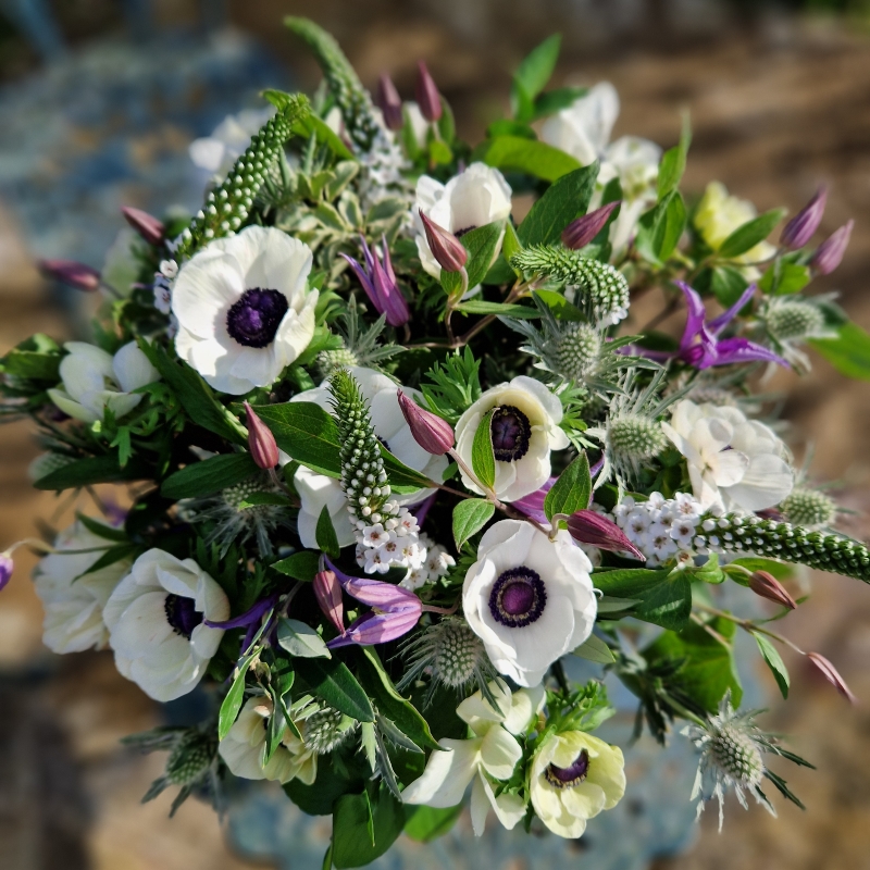 Spring bouquet with white Mistral Anemones, purple Clematis, Lysimachia, and white sea holly, inspired by East Dean’s cottage gardens and coastal charm.