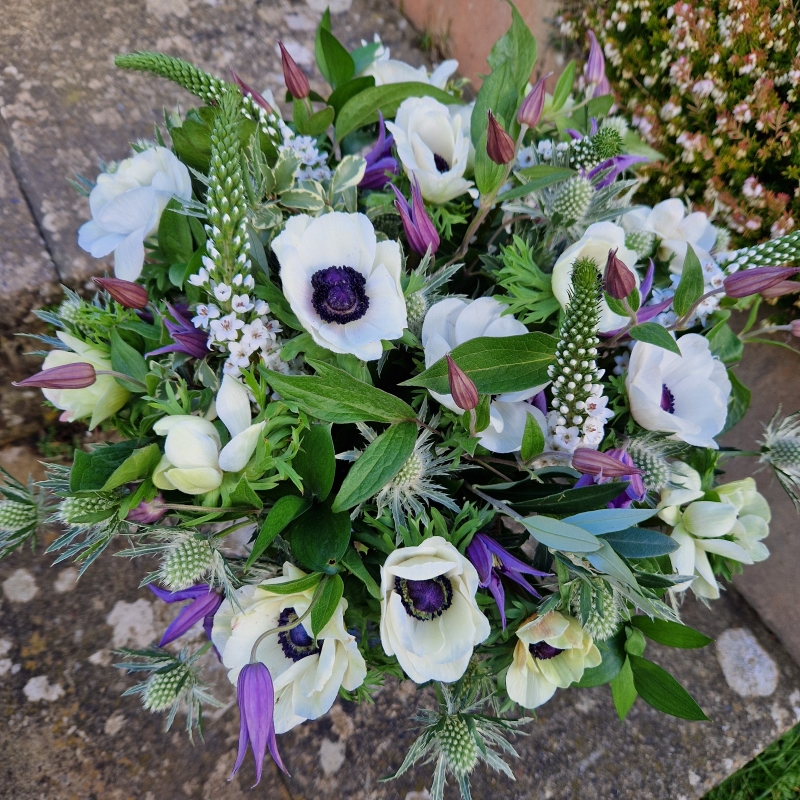 Spring bouquet with white Mistral Anemones, purple Clematis, Lysimachia, and white sea holly, inspired by East Dean’s cottage gardens and coastal charm.