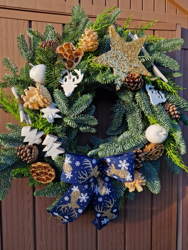 White and gold Christmas wreath with navy stag ribbon, gold sisal star, white coco trees, pine cones, lotus pods, waxed apples, and fresh pine on a moss ring.