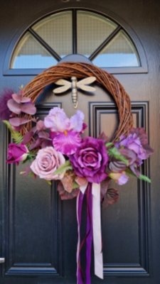 Handmade faux flower wreath in rich plum and pink tones, featuring flag iris, roses, and trailing ribbons, displayed on a black door with a metallic dragonfly ornament