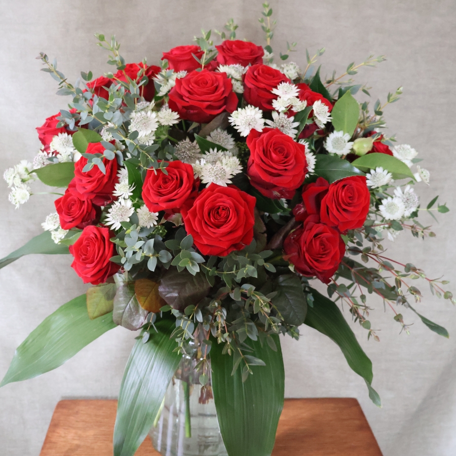 A hand‑tied luxury Valentine’s bouquet of premium red roses, delicate white Astrantia and natural foliage, gift‑wrapped and presented in a kraft water‑holding bouquet box.