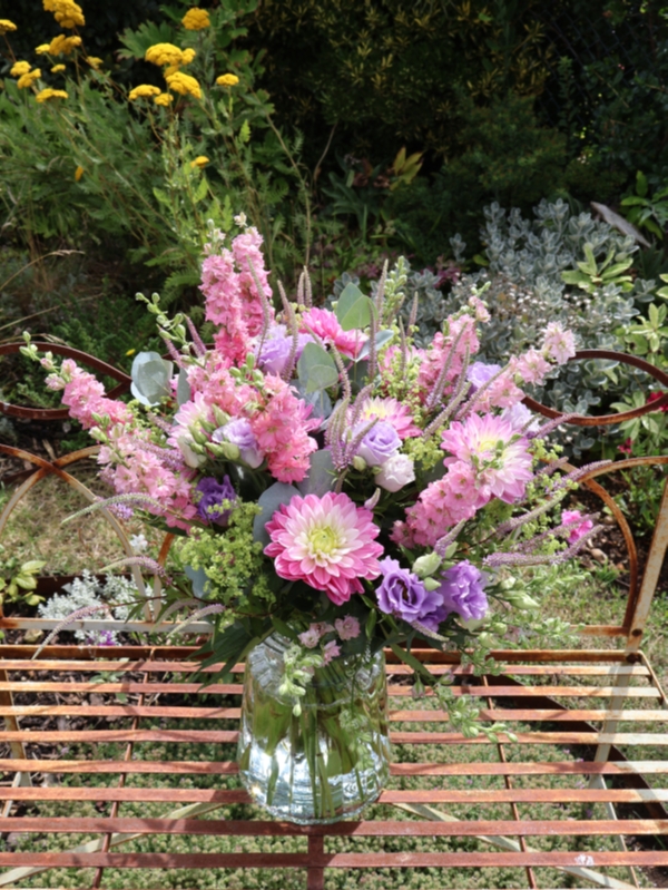 Summer garden bouquet in soft pinks and lilacs, featuring dahlia, delphinium larkspur, veronica, lisianthus, and alchemilla, styled in a wild, seasonal arrangement.