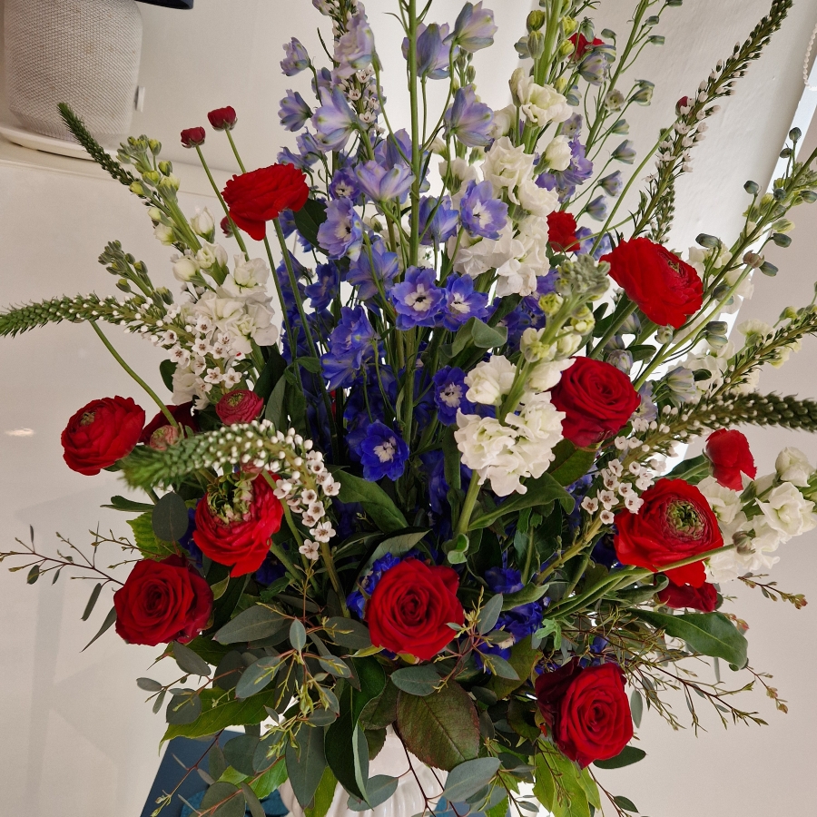 A bold statement arrangement of red, white and blue seasonal flowers, styled with height and movement and presented in a decorative urn.