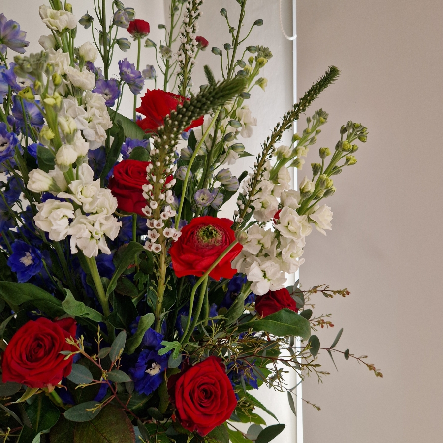 A bold statement arrangement of red, white and blue seasonal flowers, styled with height and movement and presented in a decorative urn.