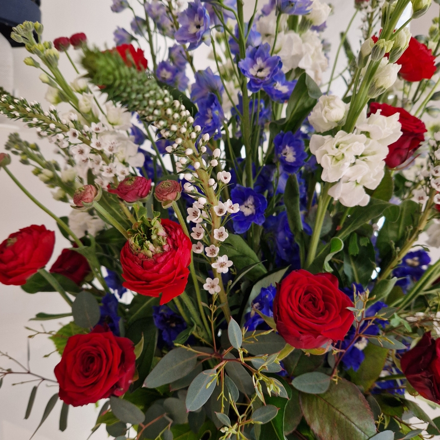A bold statement arrangement of red, white and blue seasonal flowers, styled with height and movement and presented in a decorative urn.