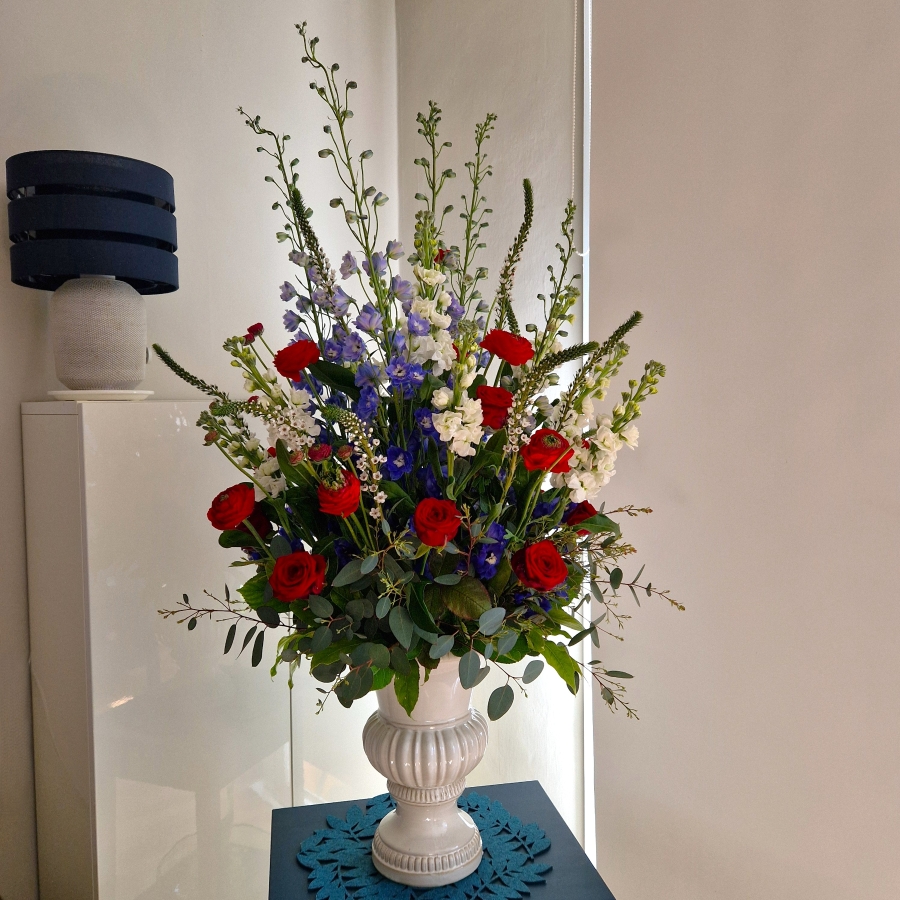 A bold statement arrangement of red, white and blue seasonal flowers, styled with height and movement and presented in a decorative urn.