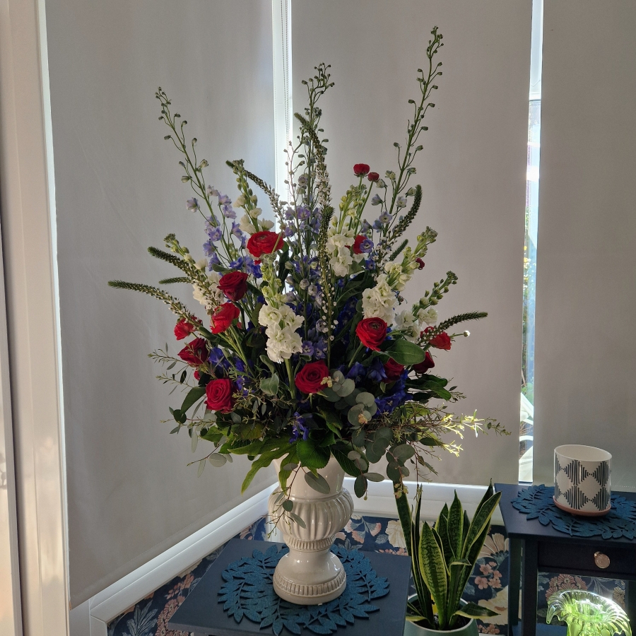 A bold statement arrangement of red, white and blue seasonal flowers, styled with height and movement and presented in a decorative urn.