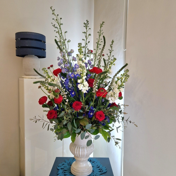 A bold statement arrangement of red, white and blue seasonal flowers, styled with height and movement and presented in a decorative urn.