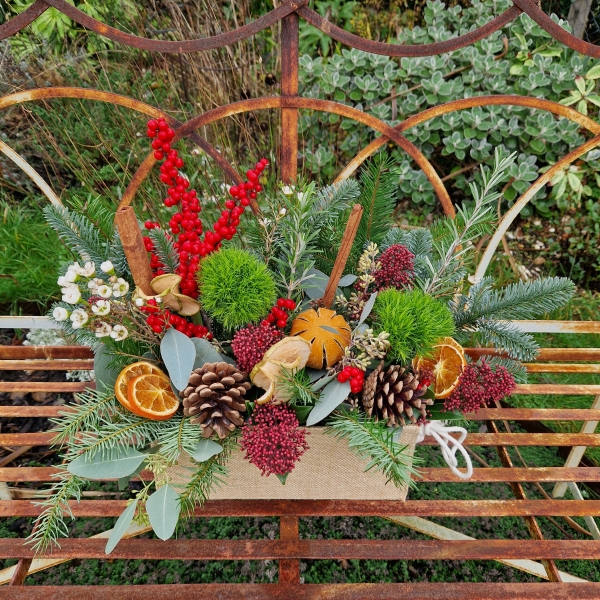 Winter arrangement in a hessian trough with pine, ilex berries, dried oranges, cinnamon sticks, pine cones, wax flower, and natural foliage.