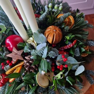 Traditional Christmas centrepiece with candles, fresh pine, holly, mixed foliage, dried fruits, chillies, oranges, apples, pine cones, pumpkins, and berries.