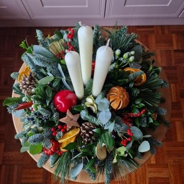 Traditional Christmas centrepiece with candles, fresh pine, holly, mixed foliage, dried fruits, chillies, oranges, apples, pine cones, pumpkins, and berries.