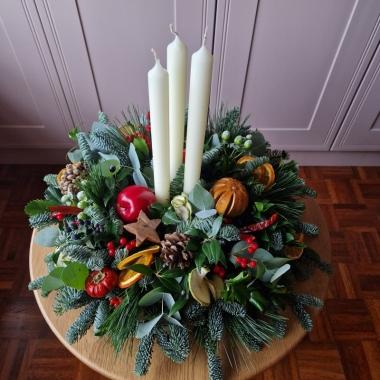 Traditional Christmas centrepiece with candles, fresh pine, holly, mixed foliage, dried fruits, chillies, oranges, apples, pine cones, pumpkins, and berries.
