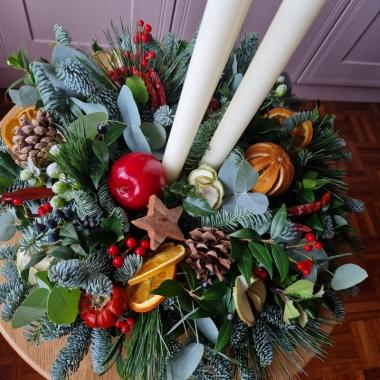 Traditional Christmas centrepiece with candles, fresh pine, holly, mixed foliage, dried fruits, chillies, oranges, apples, pine cones, pumpkins, and berries.