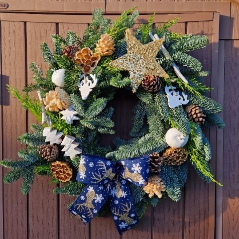 White and gold Christmas wreath with navy stag ribbon, gold sisal star, white coco trees, pine cones, lotus pods, waxed apples, and fresh pine on a moss ring.