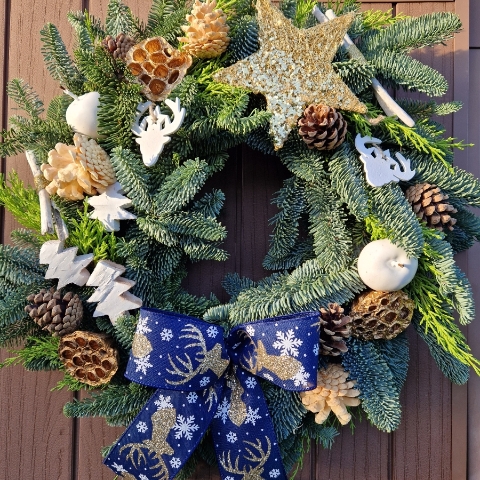 White and gold Christmas wreath with navy stag ribbon, gold sisal star, white coco trees, pine cones, lotus pods, waxed apples, and fresh pine on a moss ring.