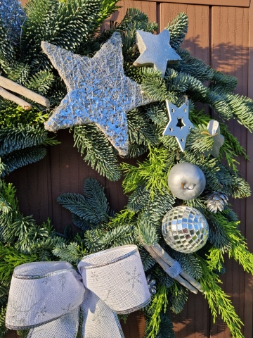 Christmas door wreath with fresh pine, conifers, silver sisal star, wooden and coco stars, waxed apples, pine cones, and mirror baubles.