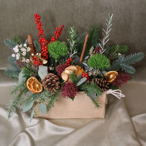 Winter arrangement in a hessian trough with pine, ilex berries, dried oranges, cinnamon sticks, pine cones, wax flower, and natural foliage.