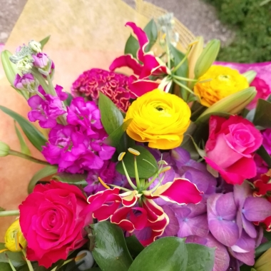 Brighton Bloom summer bouquet featuring vivid gloriosa, hot pink roses and celosia, golden achillea, purple scented matthiola, and large hydrangea—arranged with dramatic colour contrasts - inspired by a vibrant seafront.